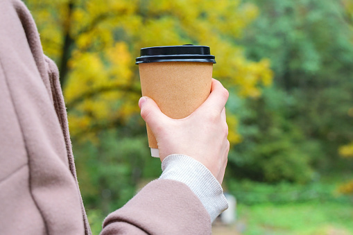 Woman holding a hot paper cup with coffee or tea in autumn