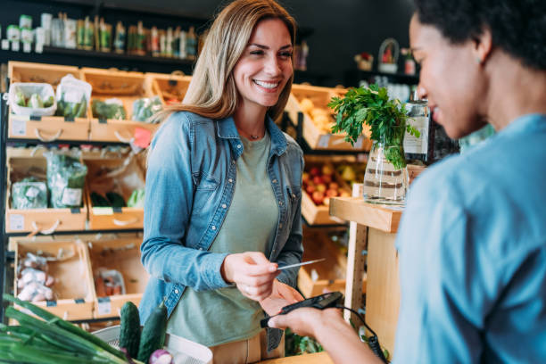 Customer paying bill using a credit card. Shot of a female customer making wireless or contactless payment using debit or credit card. Woman paying for groceries at checkout in organic store. paying stock pictures, royalty-free photos & images