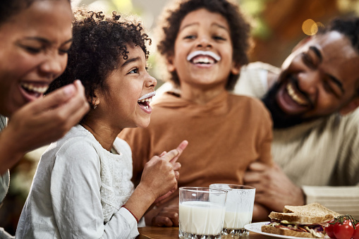 Happy African American kids having milk mustache while having breakfast with their parents in dining room. Focus is on girl.