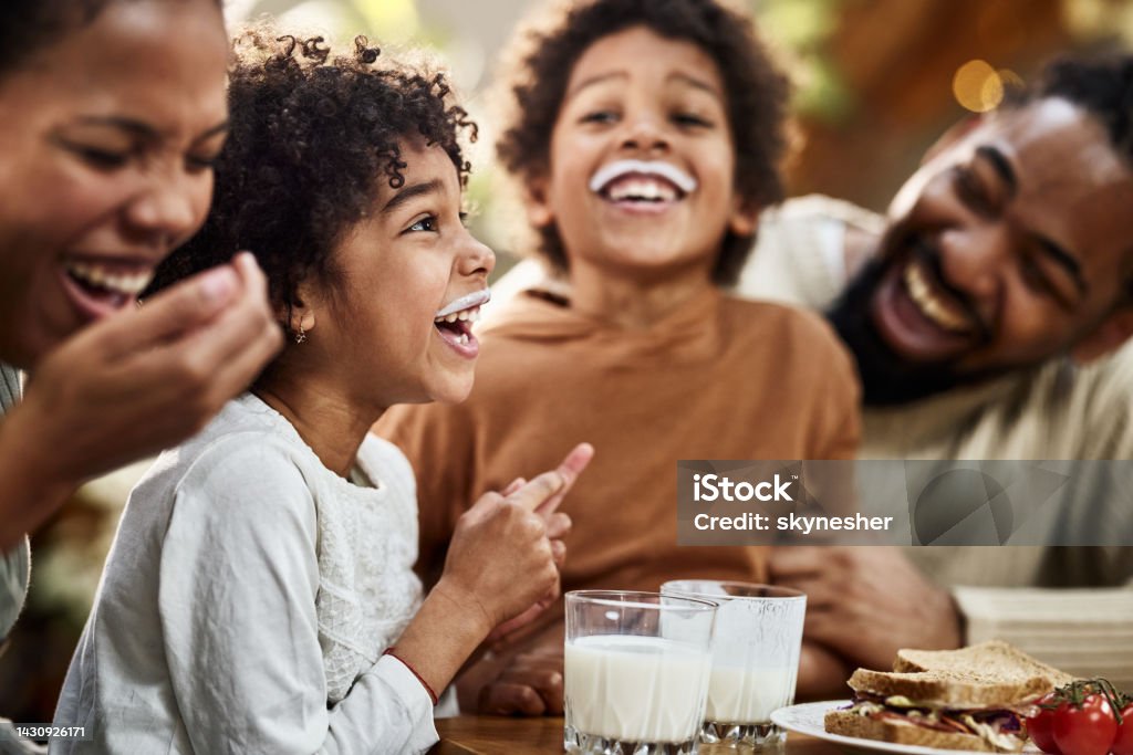 We both have milk mustache! Happy African American kids having milk mustache while having breakfast with their parents in dining room. Focus is on girl. Eating Stock Photo