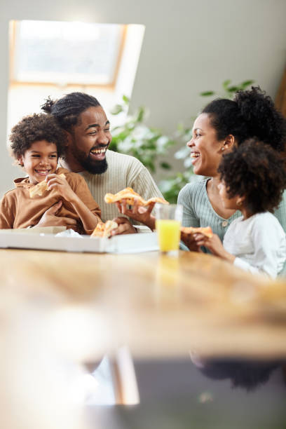 wesoła czarna rodzina rozmawiająca podczas jedzenia pizzy na lunch w jadalni. - pizza eating african descent lunch zdjęcia i obrazy z banku zdjęć