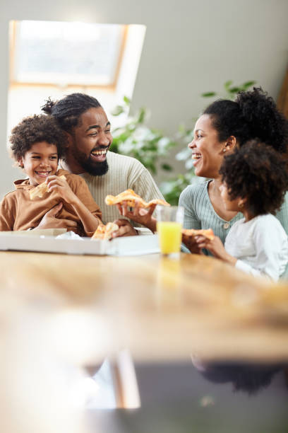 cheerful black family talking while eating pizza for lunch in dining room. - pizza eating african descent lunch imagens e fotografias de stock