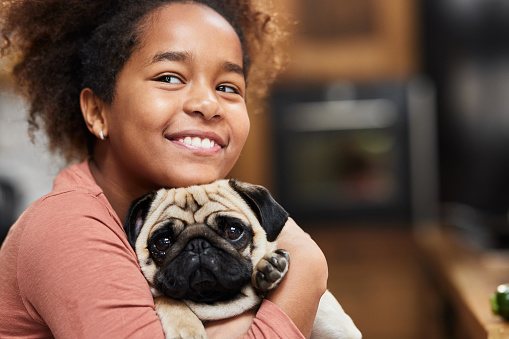 Happy African American girl embracing her pug at home.
