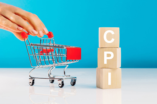 CPI - Consumer Price Index symbol.Letter block in word CPI abbreviation of consumer price index and woman's hand pushing empty shopping cart on blue background. Business and CPI, consumer price index concept