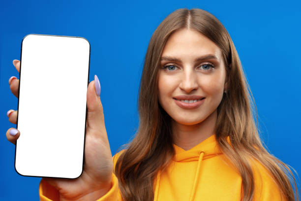 istock Young woman showing big blank cellphone screen on blue background in studio 1430931083