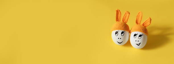 deux œufs blancs en bonnet orange avec des oreilles de lapin et des visages joyeux sur fond jaune - easter bonnets photos photos et images de collection