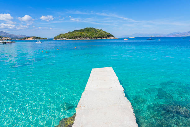 wooden walkway over the crystal clear waters with an islet in the background of the paradisiacal beach of Ksamil in Albania. stock photo
