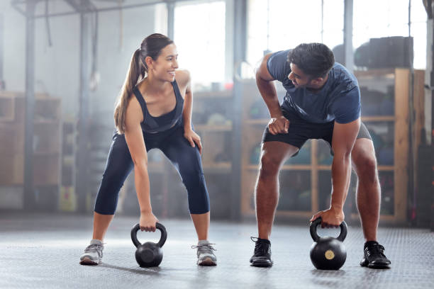 ケトルベルの体重運動、トレーニング、ジム内でトレーニングを行う強くてウェルネスなカップル。幸せなスポーツマンやトレーナーのモチベーション、筋肉、強さや健康のためのフィット� - エクササイズをする ストックフォトと画像