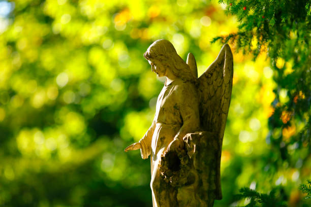 Close-up of a small old and weathered angel standing on a gravestone. Green meadow in the background.