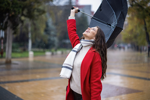 Woman in red coat raising umbrella in the air and smiling