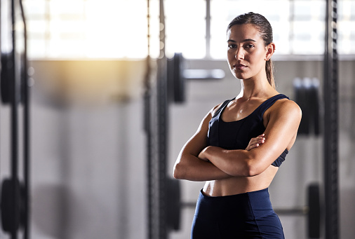 Fit, slim and serious woman with arms crossed, feeling confident about her body and health while standing in gym. Portrait of a sporty and determined woman ready to exercise to stay in healthy shape