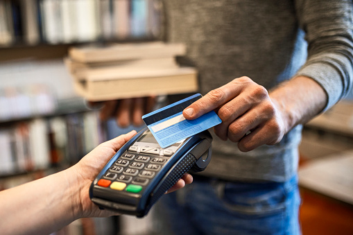 Young man paying with a credit card for book at the modern bookstore