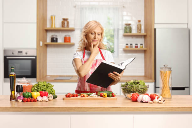 istock Housewife reading from a cook book and standing behind a kitchen counter 1430946444
