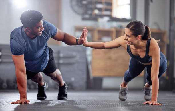 Fitness, motivation and high five while doing push ups and exercising together at the gym. Healthy, fit and athletic couple goals while enjoying a training session with teamwork at a health club