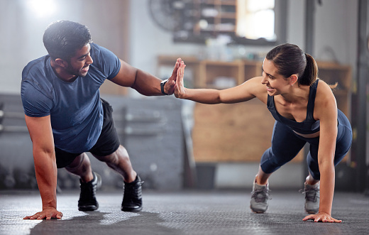 Fitness, motivation and high five while doing push ups and exercising together at the gym. Healthy, fit and athletic couple goals while enjoying a training session with teamwork at a health club