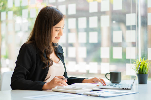 istock Asian businesswoman with chart or document at work using business laptop calculator financial accountant calculating money 1430951884