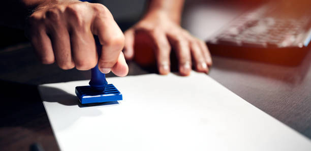 istock Man's hand stamping with approved stamp on document paper at desk. 1430953978