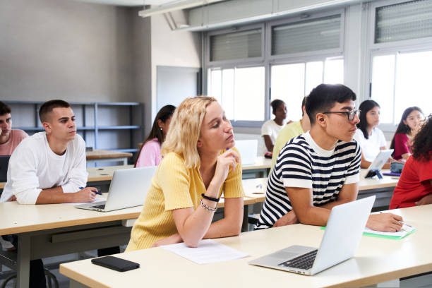 istock High school science class: A boy and girl using a laptop computer while attending to the teacher in class. Group of students learning in the classroom. 1430955887