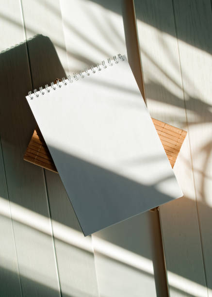 istock An open blank notepad is on a wooden crate on a white table. The shadows of plants fall on the paper. Notepad mockup. Natural light from the window. Top view. Flat lay. Copy space. 1430956659