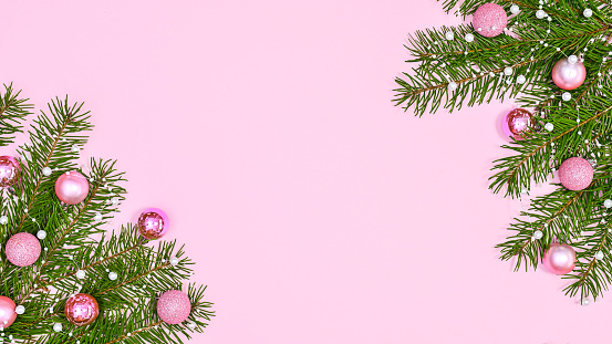Beautiful Chrismtas background with pastel pink ornaments on fir branches on pastel pink theme. FLat lay