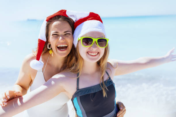 smiling mother and child in santa hat at beach having fun time stock photo