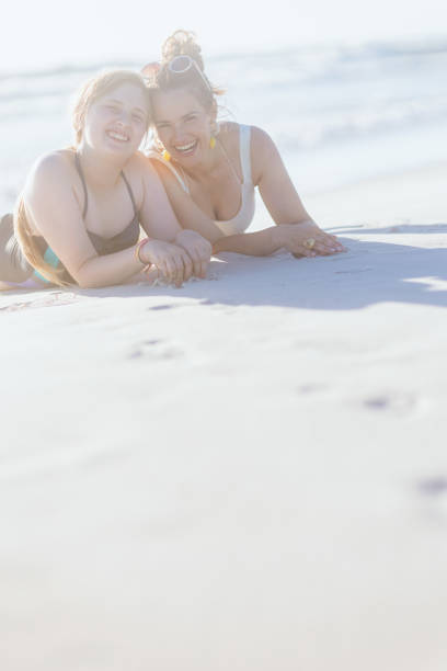 улыбающаяся современная мать и дочь-подросток лежат на пляже - teenager parent beach contemporary стоковые фото и изображения