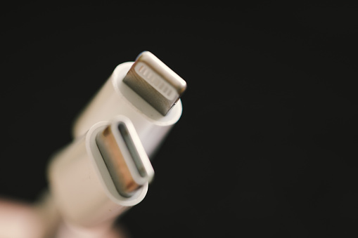 Macro close up depicting a person holding a USB-C to Lightning charging cable. Focus on the cable with the background defocused.