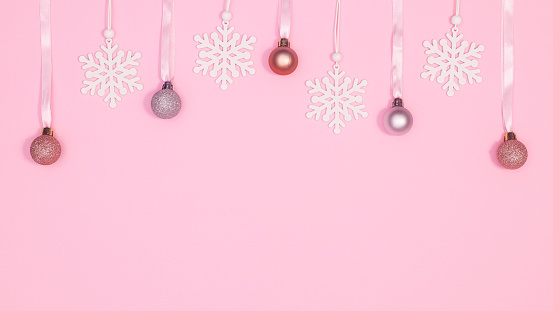 Hanging Christmas ornaments and snowflakes on pastel pink background with copy space