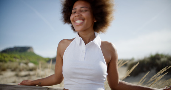Young african girl with afro hair laughing with closed eyes. Portrait shot. Landscape background. Focus on foreground.