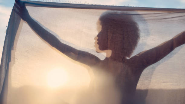 Silhouette of woman behind curtain in sunset on the beach. Blurred portrait. stock photo