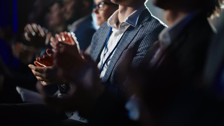 Close Up on Hands of an Audience of People Applauding in Dark Concert Hall During a Business Conference Presentation. Technology Summit Auditorium Room Full of Corporate Delegates.