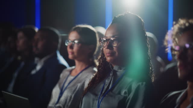 Portrait of a Beautiful Black Female Sitting in a Dark Crowded Auditorium at a Tech Conference. African Woman Listening to an Inspiring Keynote Presentation. Specialist Interested in New Technology.