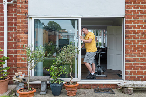 Man getting ready to do a home workout in his living room in the North East of England. He has set up an electric bike facing out into his garden with a patio door open for fresh air.