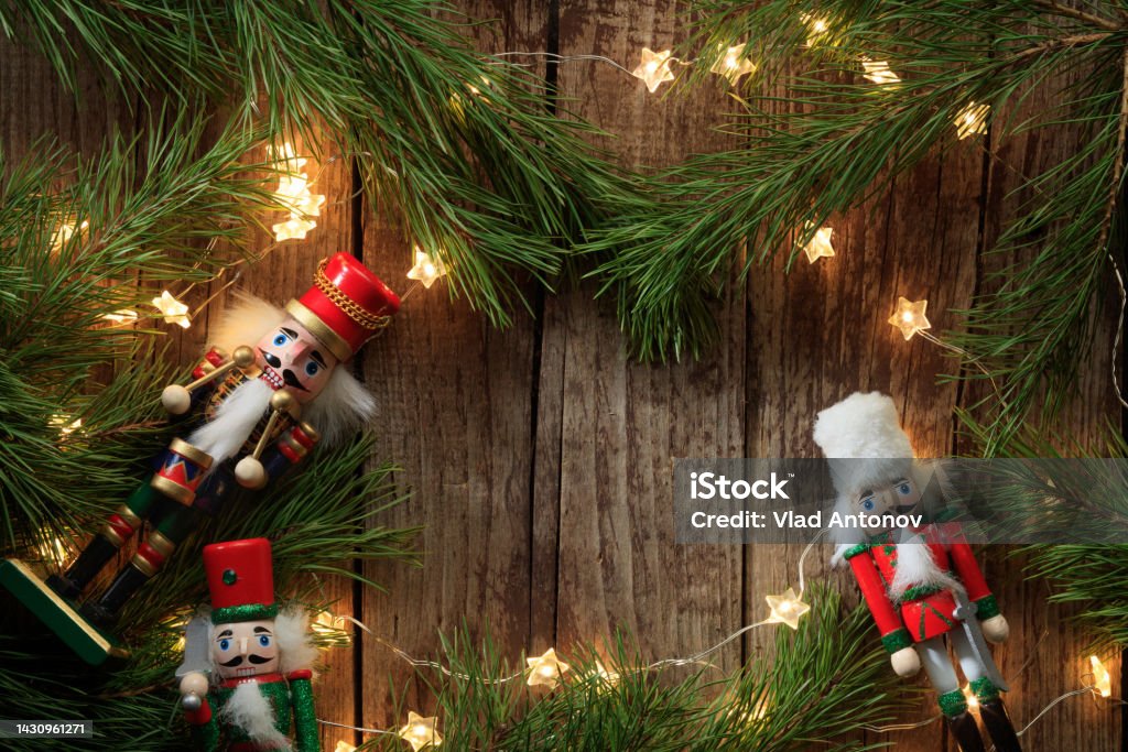 Christmas composition of coniferous branches, Nutcrackers toys and lighting garlands Christmas composition of coniferous branches, Nutcrackers toys and lighting garlands on old wooden boards . Top view. Nature New Year concept. Nutcracker Stock Photo