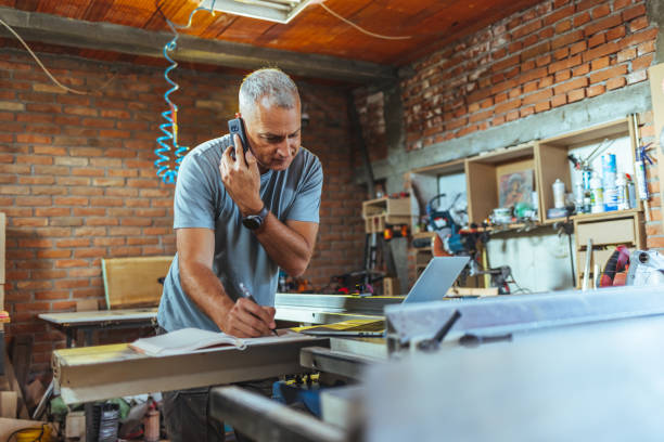 istock Mature worker using laptop and speaking by smartphone in workshop interior, copy space 1430966301