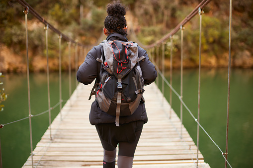 Rear view of a woman with a backpack crossing a bridge.