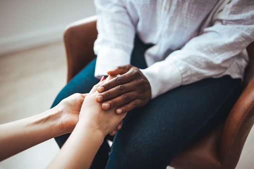 Biracial female psychologist hands holding palms of millennial woman patient. Cropped image of woman comforting her friend. Shot of two unrecognizable women holding hands together