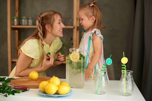 blonde woman make lemonade in kitchen with her little daughter, mother calms her child. shallow depth of field photo