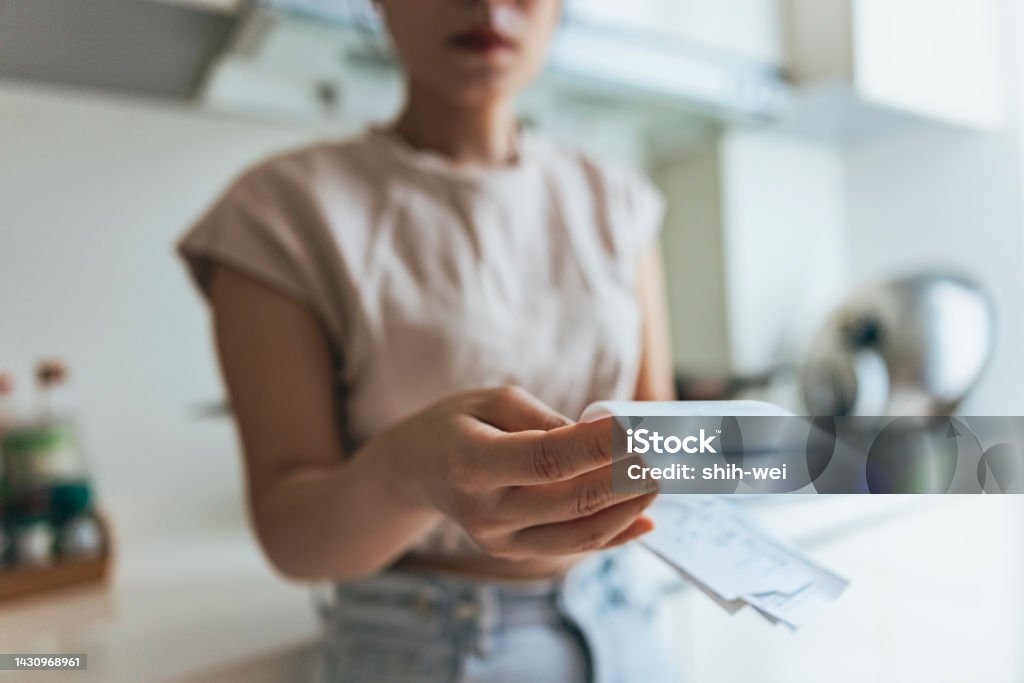 Asian women examining the shopping receipt at home Woman holding paper various expense bills and plans for personal finances at her home. Paycheck Stock Photo