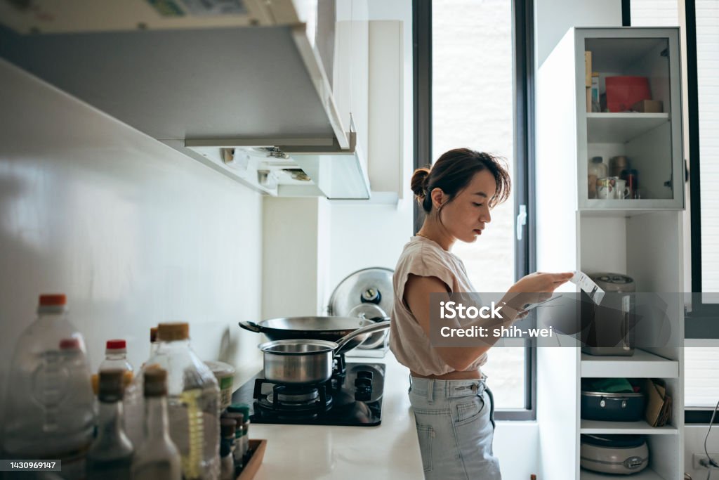 Asian women examining the shopping receipt at home Woman holding paper various expense bills and plans for personal finances at her home. Inflation - Economics Stock Photo