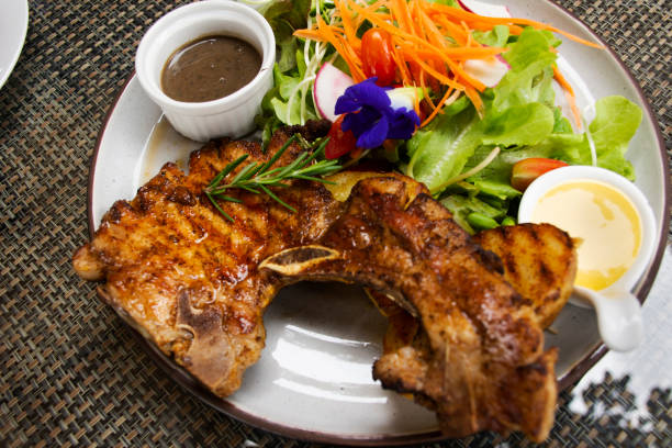 Thai chef cooking food fusion style cuisine roasted grilled fried Pork Chop Steak with spicy sauce and vegetables fruits salad on ceramic dish plate served at restaurant cafe shop in Bangkok, Thailand