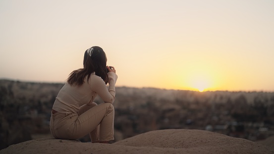 A young female tourist is taking photos and videos of nature and sunset with camera in Cappadocia Türkiye.