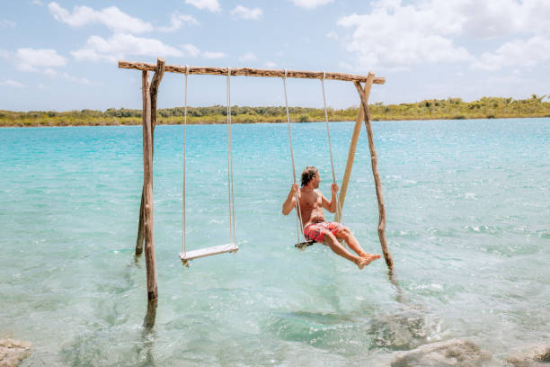 istock Young man having fun on swing in a beautiful lagoon on a sunny day 1430975199