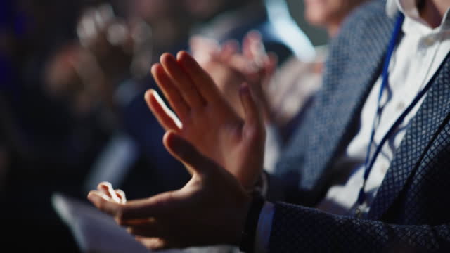 Close Up on Hands of a Crowd of People Clapping in Dark Conference Hall During a Motivational Keynote Presentation. Business Technology Summit Auditorium Room Full of Delegates.
