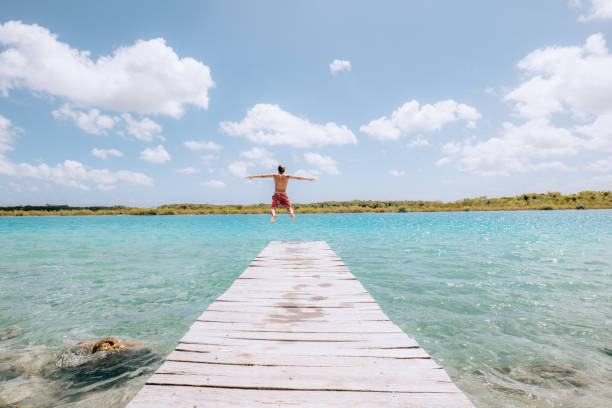 istock Happy young man jumping from pier into beautiful lake 1430975321