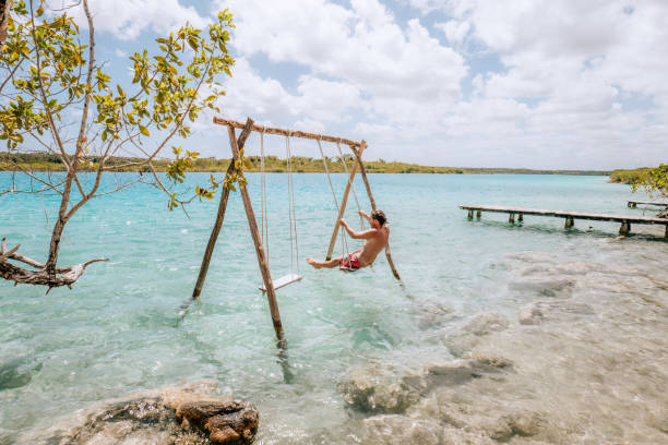 istock Young man having fun on swing in a beautiful lagoon on a sunny day 1430975423