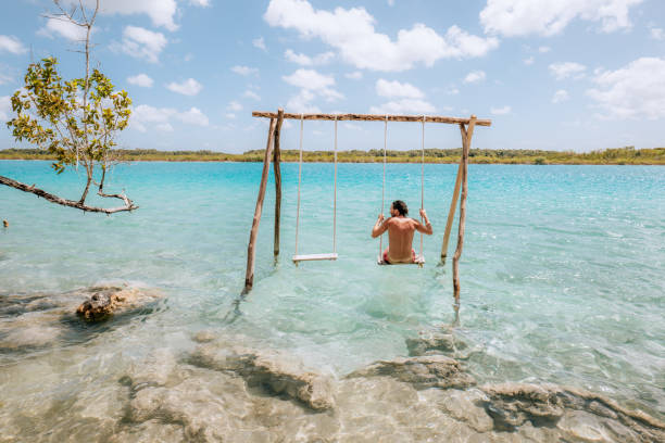 istock Young man having fun on swing in a beautiful lagoon on a sunny day 1430975485