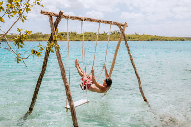 istock Young man having fun on swing in a beautiful lagoon on a sunny day 1430975489