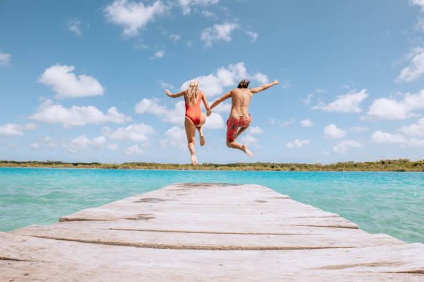 Couple run and jump from wooden pier onto lake They enjoy nature peace and tranquillity on a jetty bay the lake in Mexico people jumping sea beach stock pictures, royalty-free photos & images