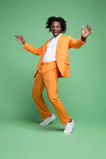 Portrait of excited elegant man Full length portrait of elegant man wearing orange suit and white shirt laughing at camera. Studio shot, green background. men hairstyle afro cool stock pictures, royalty-free photos & images